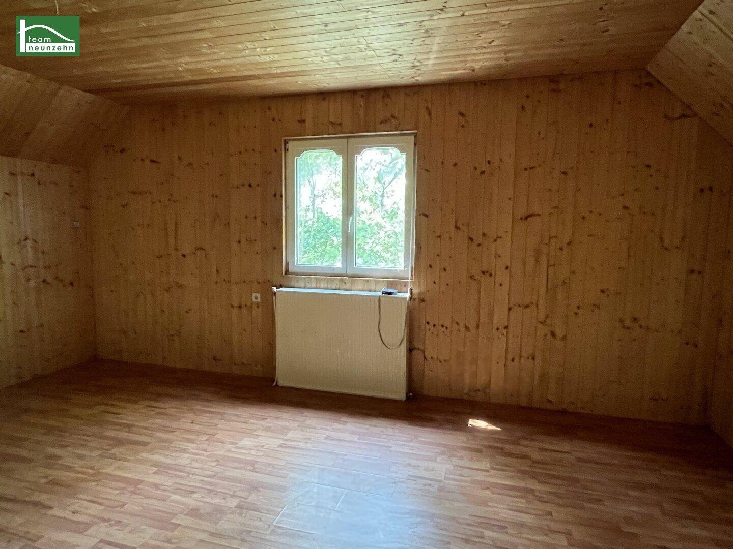 Zimmer mit Holzvertäfelung an Wänden und Decke, Laminatboden und einem Fenster.