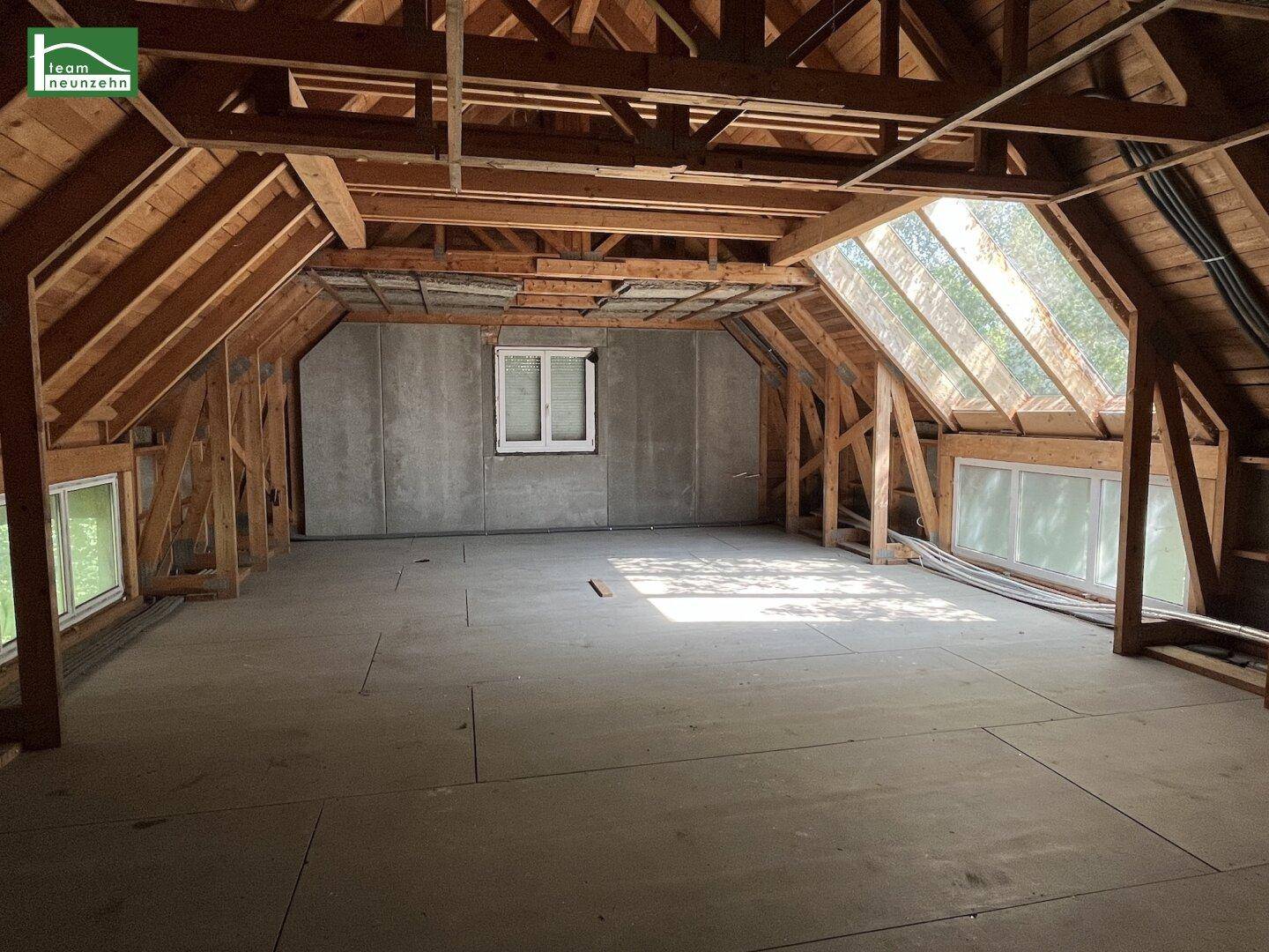 Geräumiger Dachboden mit freiliegenden Holzbalken, Dachfenstern und unfertigem Boden.