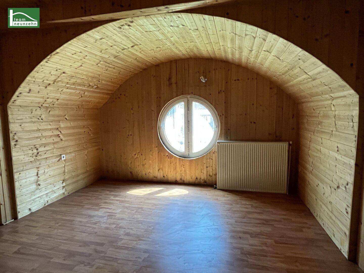 Zimmer mit gewölbter Holzdecke, Holzvertäfelung und einem einzigartigen runden Fenster.