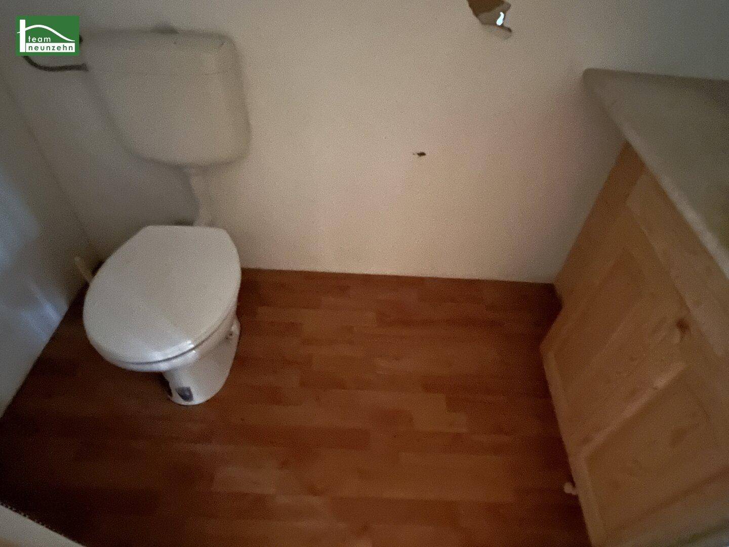 Kleines Gäste-WC mit einfacher Toilette, Waschbeckenunterschrank und Holzoptik-Laminatboden.