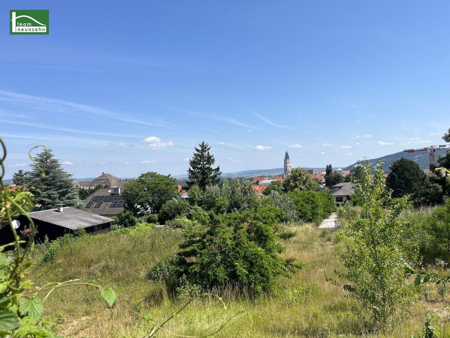 Weiter Blick über eine grüne Landschaft mit vereinzelten Häusern und einem Kirchturm unter klarem Himmel.