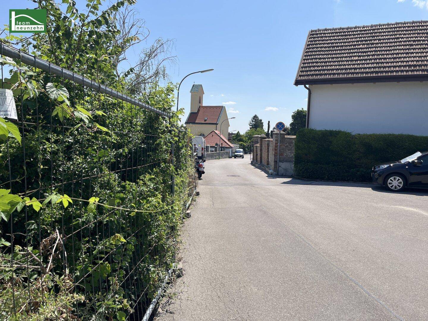 Eine ruhige Wohnstraße mit einer Kirche im Hintergrund, umgeben von grünen Hecken und Häusern.