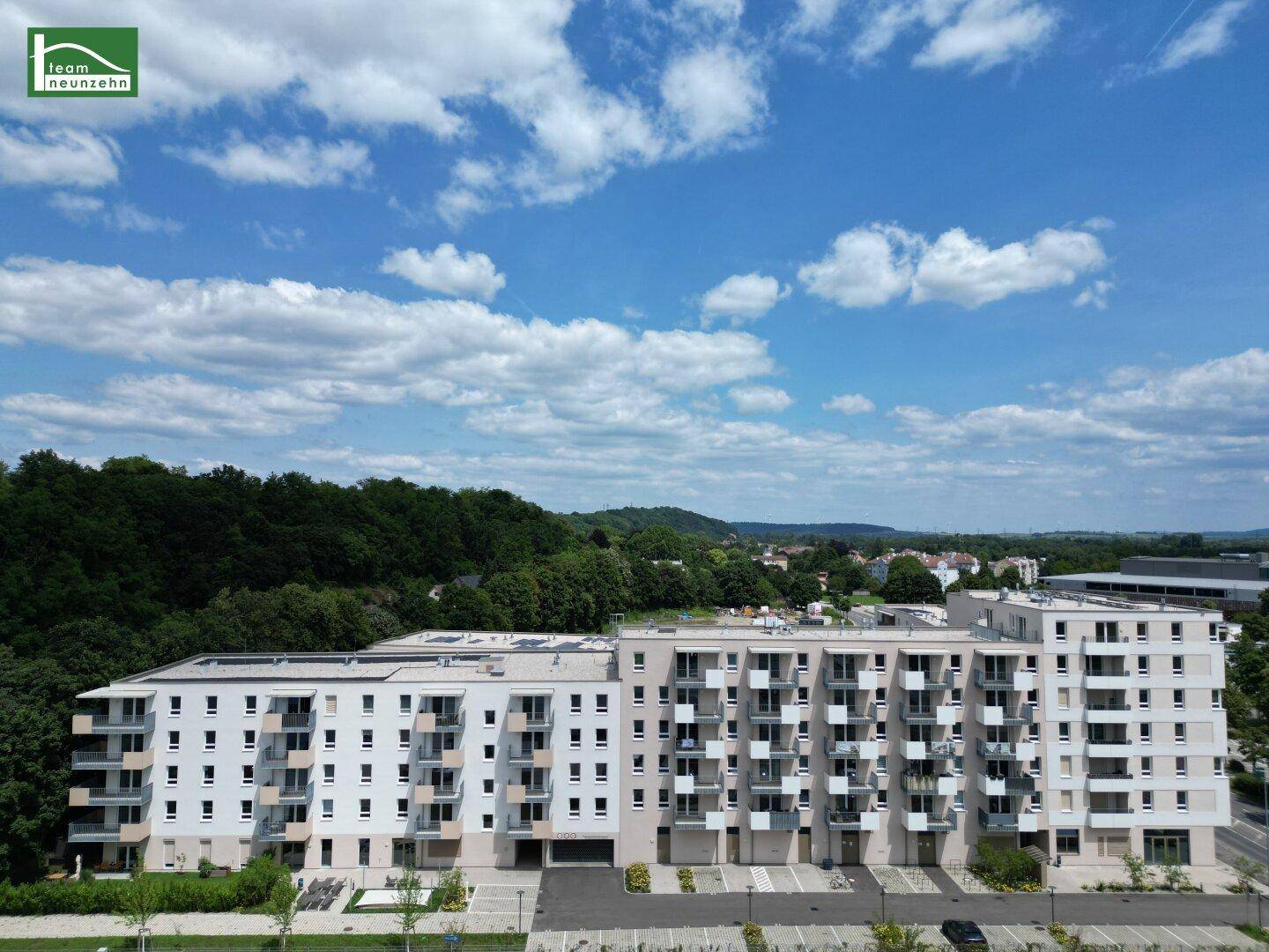 Modernes Mehrfamilienhaus mit vielen Balkonen, umgeben von viel Grün und mit Weitblick über die Landschaft.