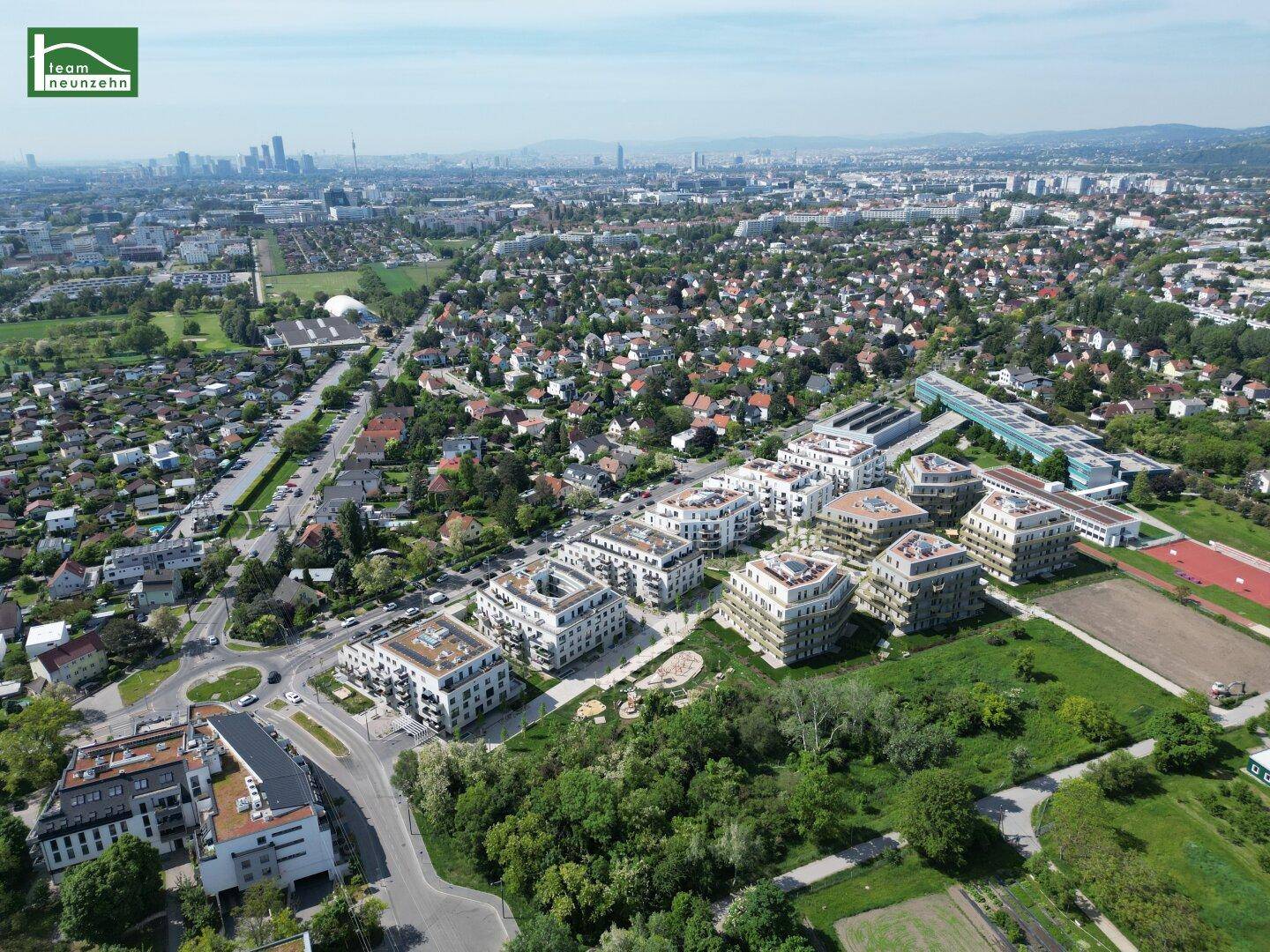 Luftaufnahme einer modernen Wohnanlage mit viel Grünfläche und Blick auf die Stadt.