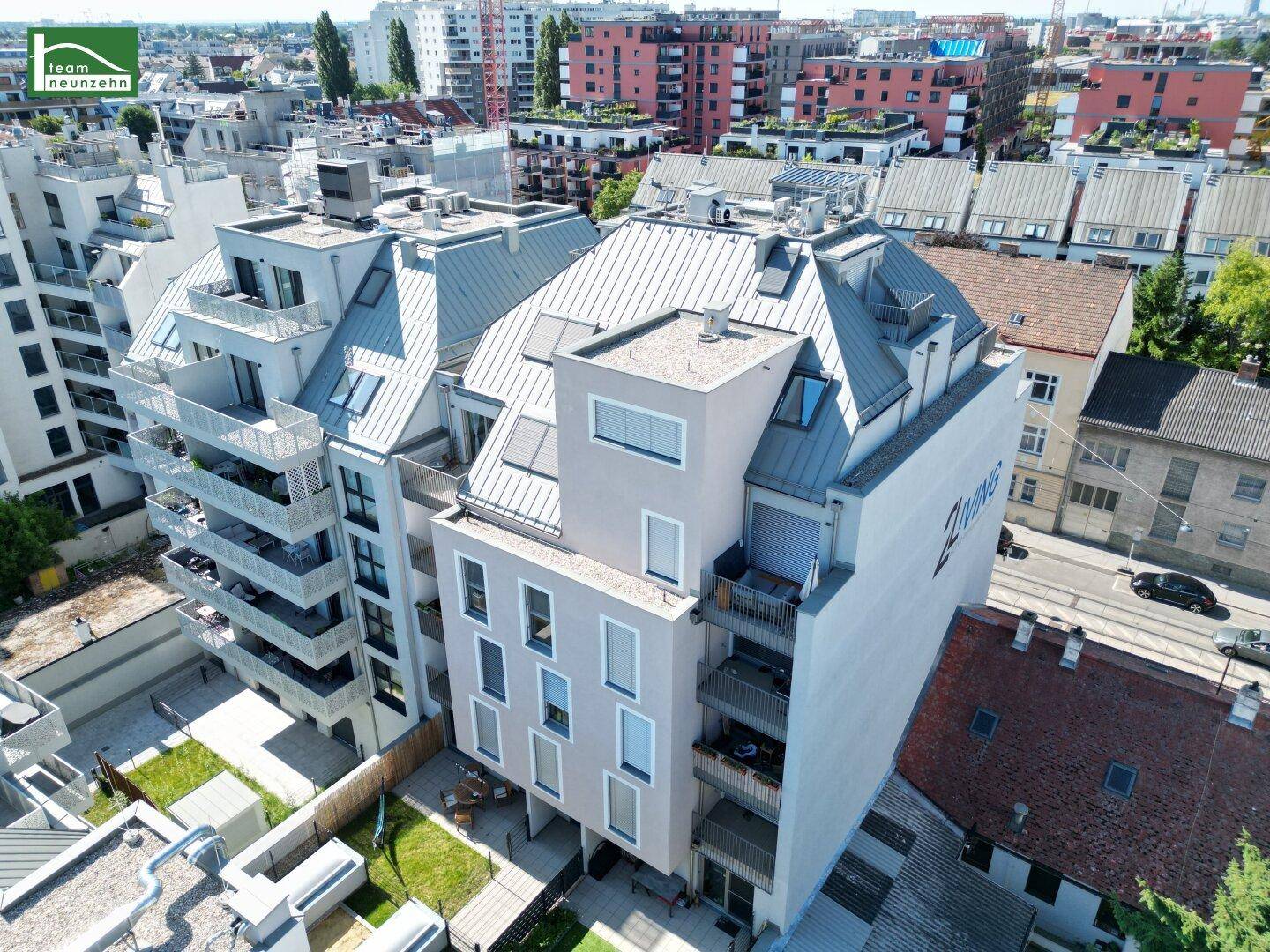 Moderne Wohnanlage aus der Vogelperspektive mit Balkonen, Dachterrassen und Grünflächen im städtischen Umfeld.
