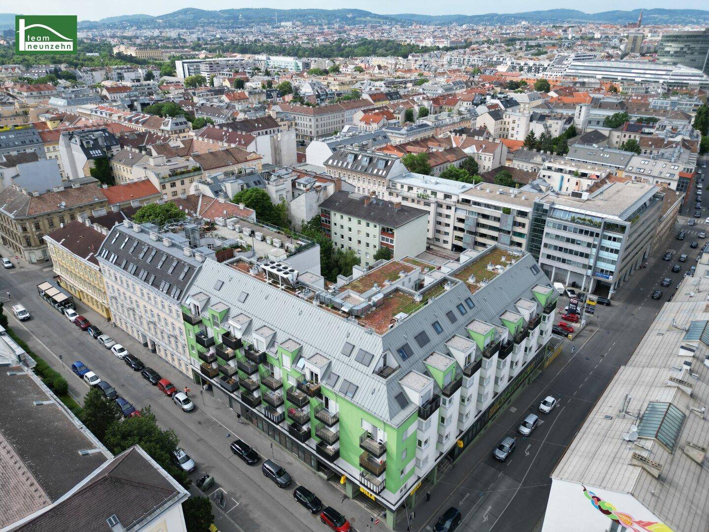 Luftaufnahme eines lebhaften Stadtviertels mit modernen Wohngebäuden und einem markanten grünen Gebäude.