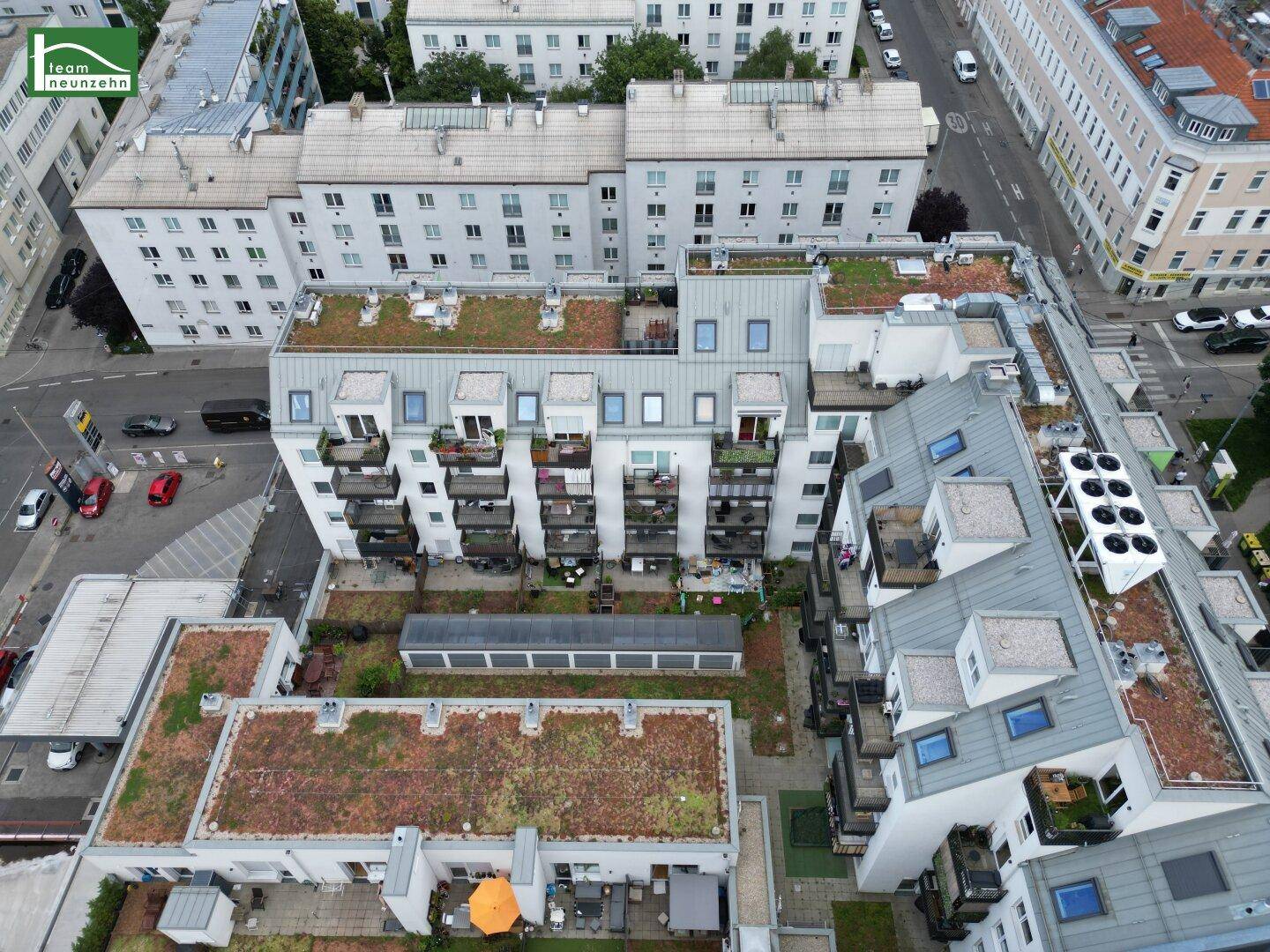 Blick von oben auf einen begrünten Innenhof mit Sitzgelegenheiten, umgeben von Gebäuden mit Balkonen.