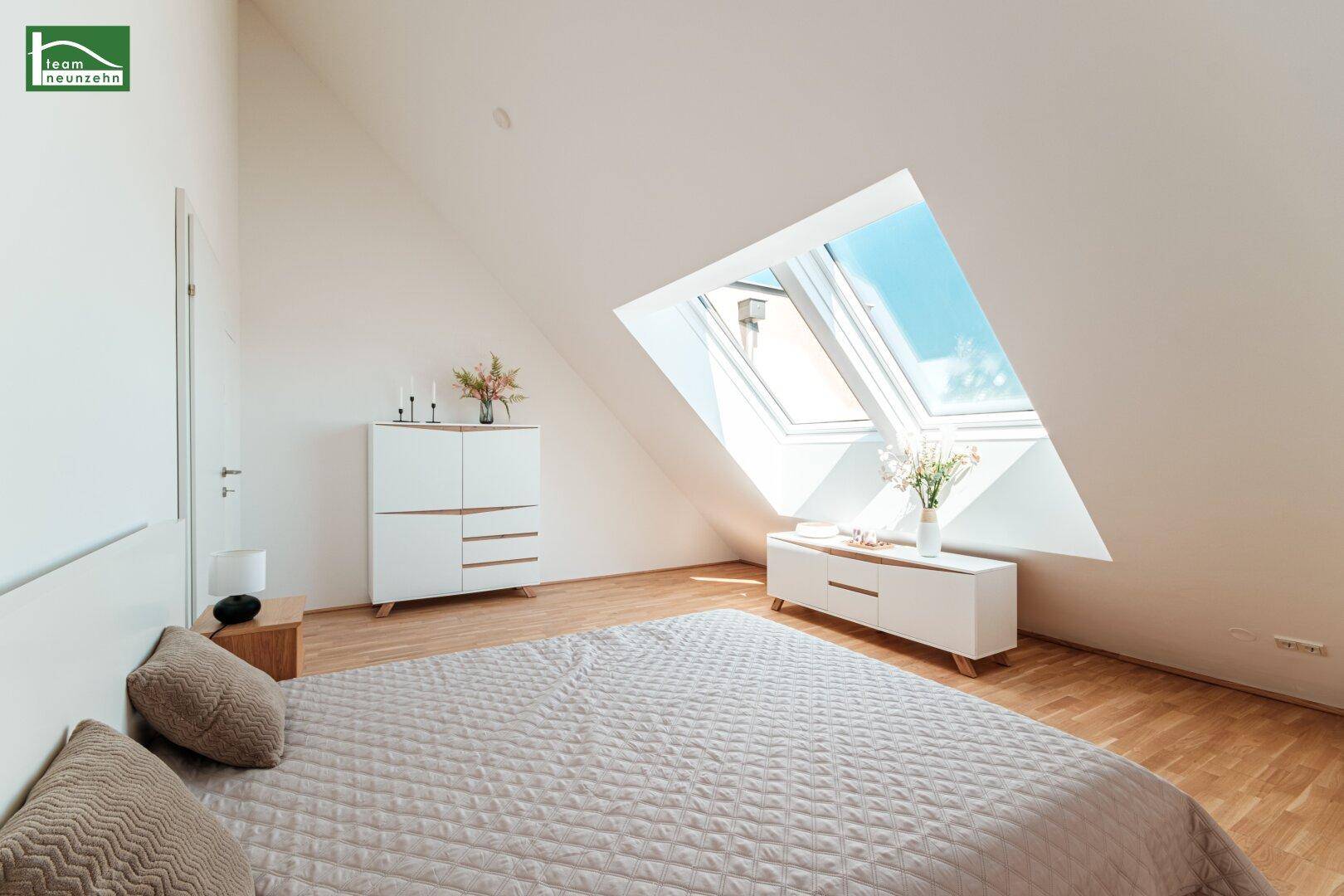 Helles Schlafzimmer im Dachgeschoss mit schrägen Wänden, Dachfenstern und modernem Holzboden.