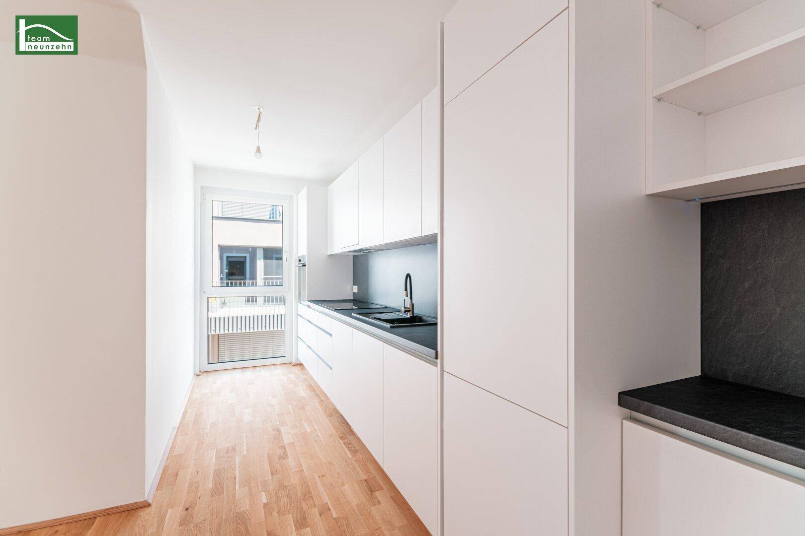 Moderne Einbauküche mit weißen Schränken, dunkler Arbeitsplatte und Fenster.