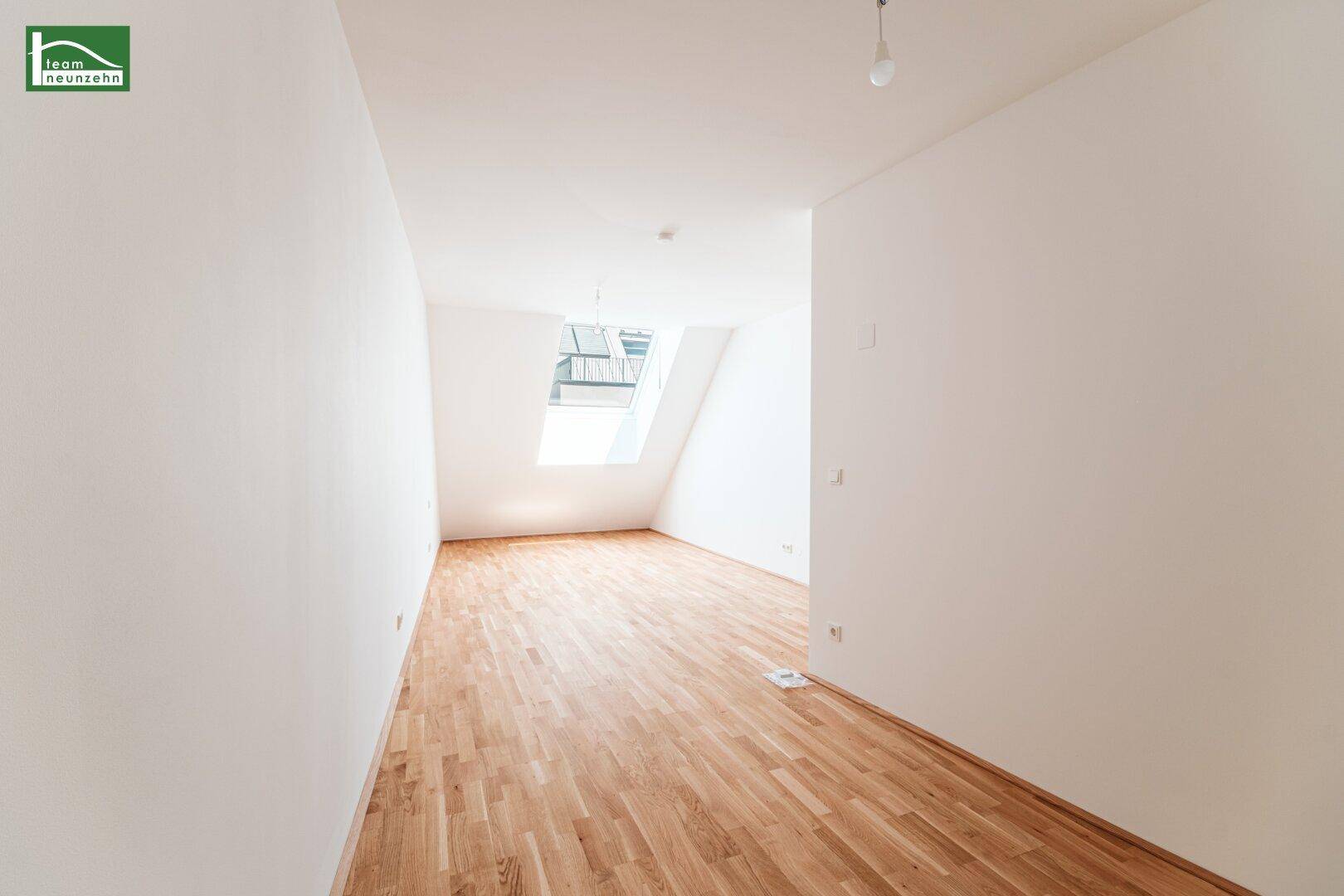 Heller Raum im Dachgeschoss mit Schrägdach, Parkettboden und Dachfenster.