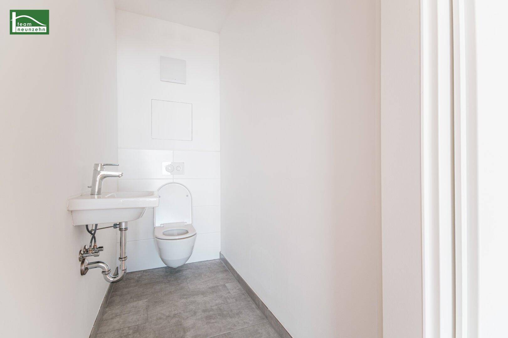 Separates Gäste-WC mit wandhängender Toilette, kleinem Waschbecken und Fliesenboden.