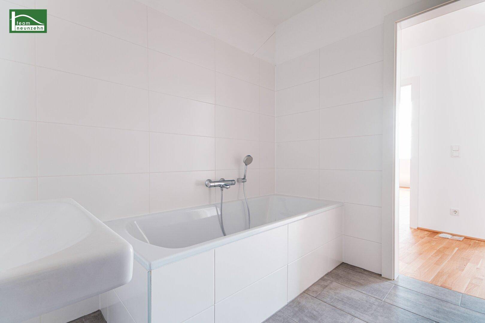 Modernes Badezimmer mit Badewanne, weißen Wandfliesen und grauem Fliesenboden.