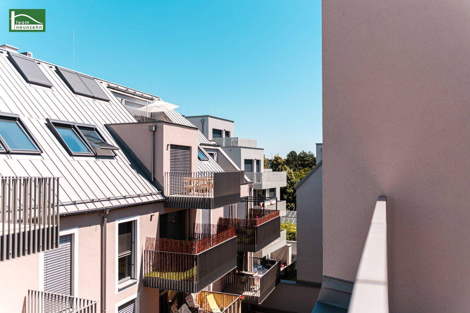 Moderne Wohngebäude mit mehreren Balkonen und Dachfenstern unter blauem Himmel.
