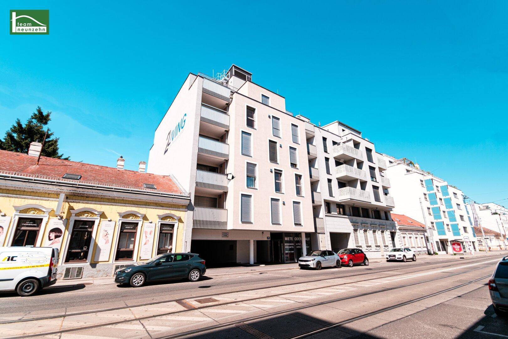 Modernes Mehrfamilienhaus mit Balkonen und großen Fenstern an einer belebten Straße.