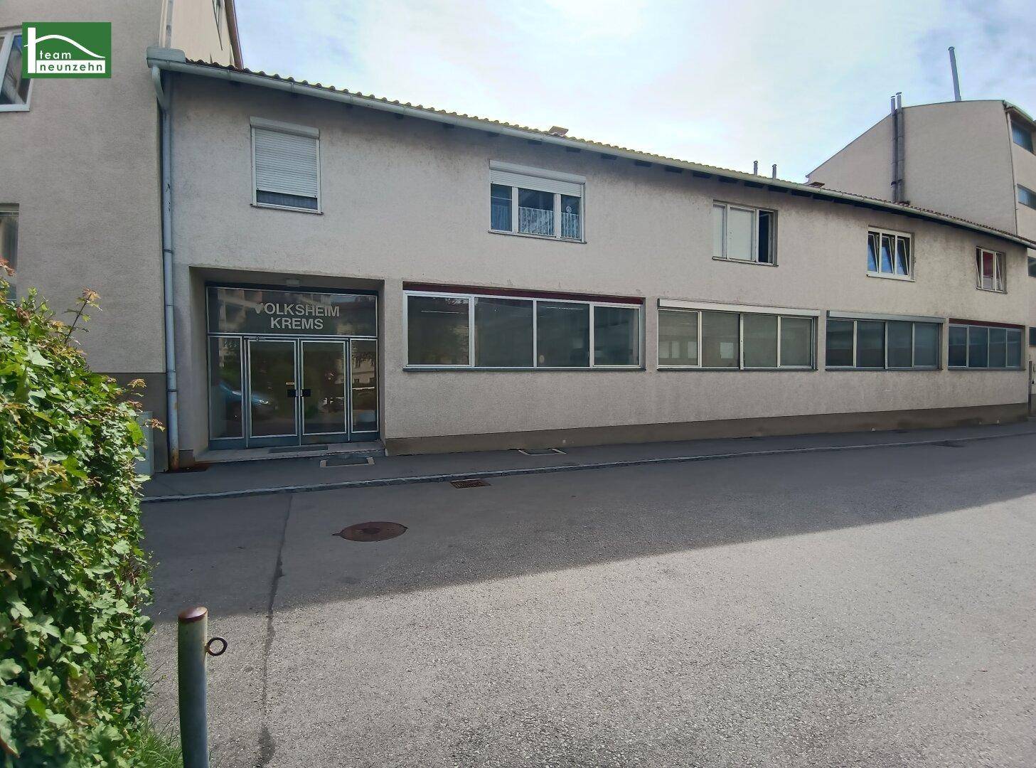 Außenansicht eines Geschäftsgebäudes mit großen Fenstern und einem Parkplatz davor.