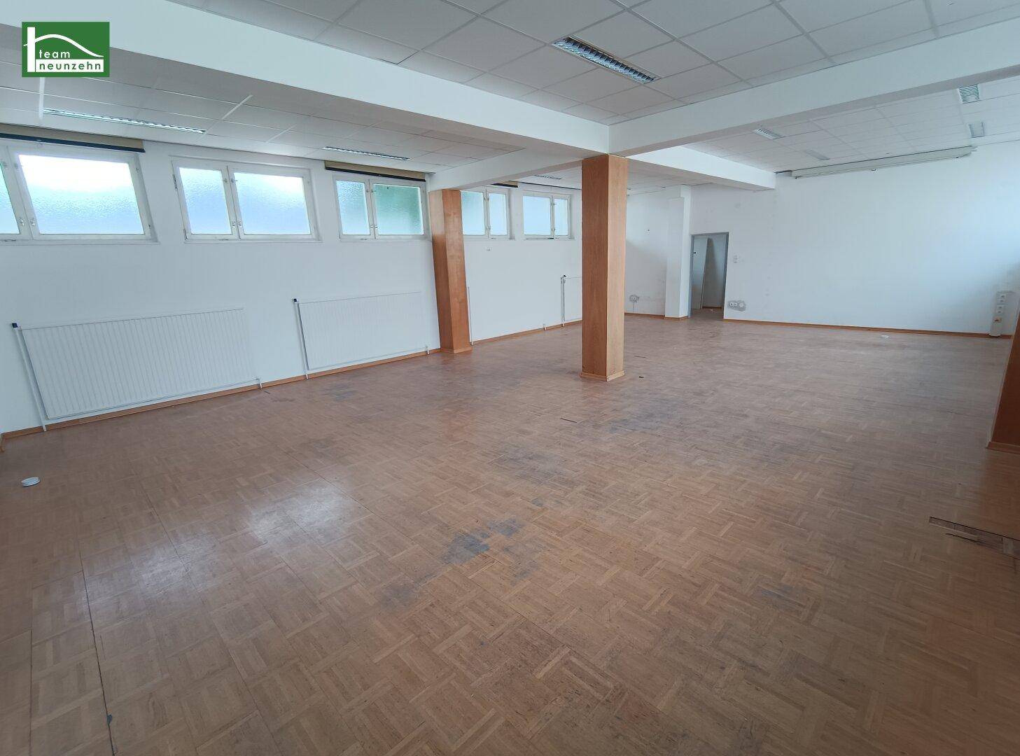 Großer, leerer Büroraum mit Holzparkettboden, vielen Fenstern und tragenden Säulen.