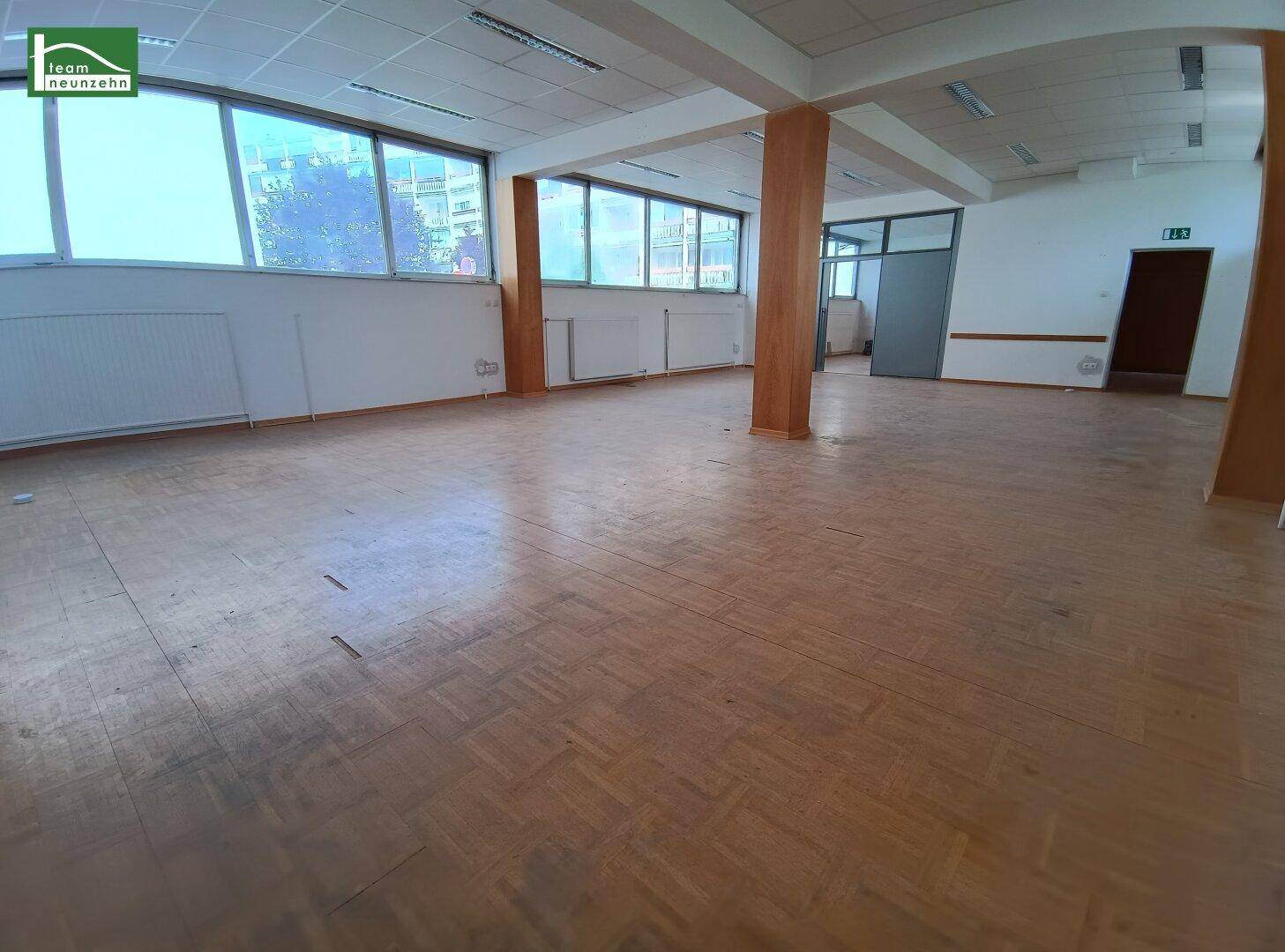 Heller, offener Büroraum mit Holzparkett, hohen Decken und vielen Fenstern für Tageslicht.