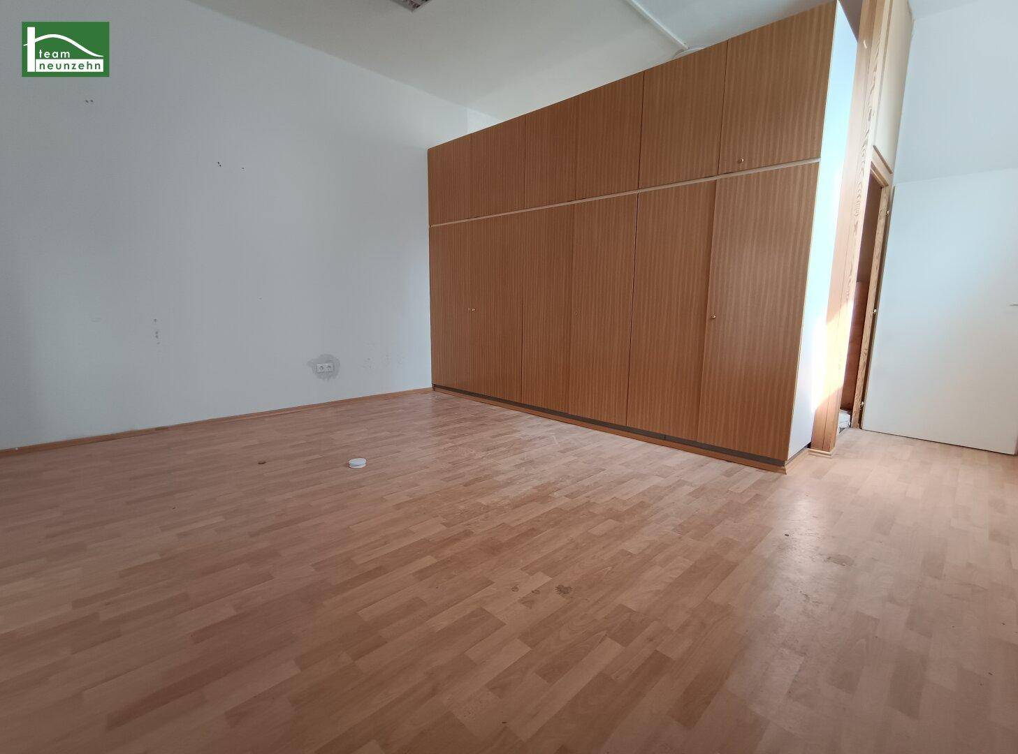Einfacher Raum mit hellem Laminatboden und einem großen, eingebauten Holzschrank.