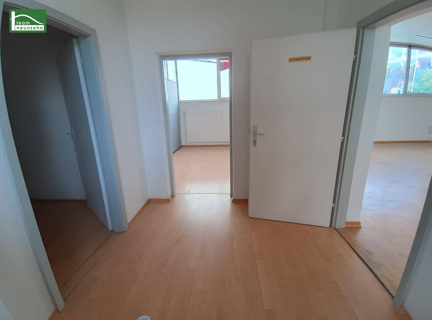 Flur mit hellem Laminatboden und mehreren Türen, darunter eine zum Toilettenbereich.