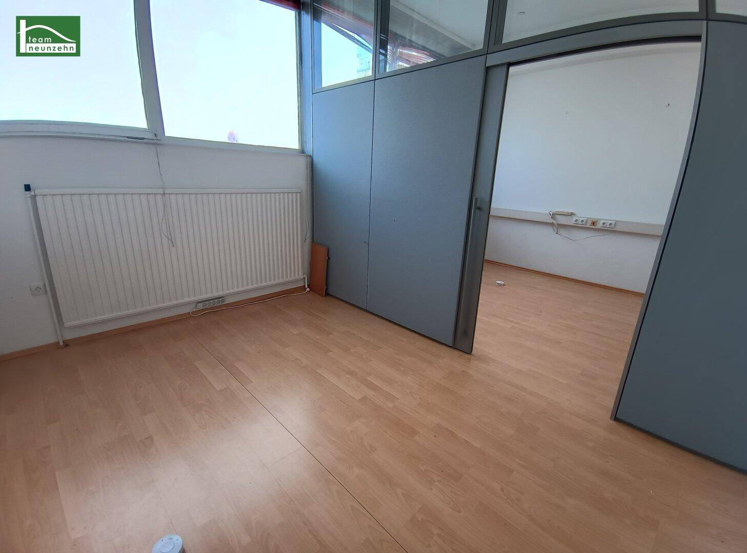 Büroraum mit Laminatboden, Fenstern und einer modernen Trennwand mit Schiebetür.