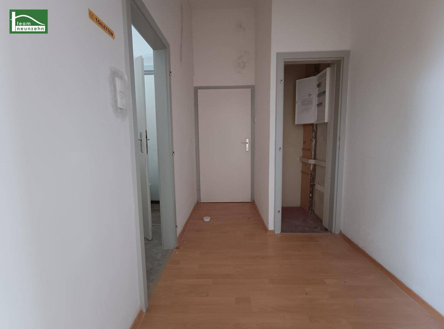 Schmaler Flur mit hellem Laminatboden und Zugang zu verschiedenen Räumen und einem Technikschrank.