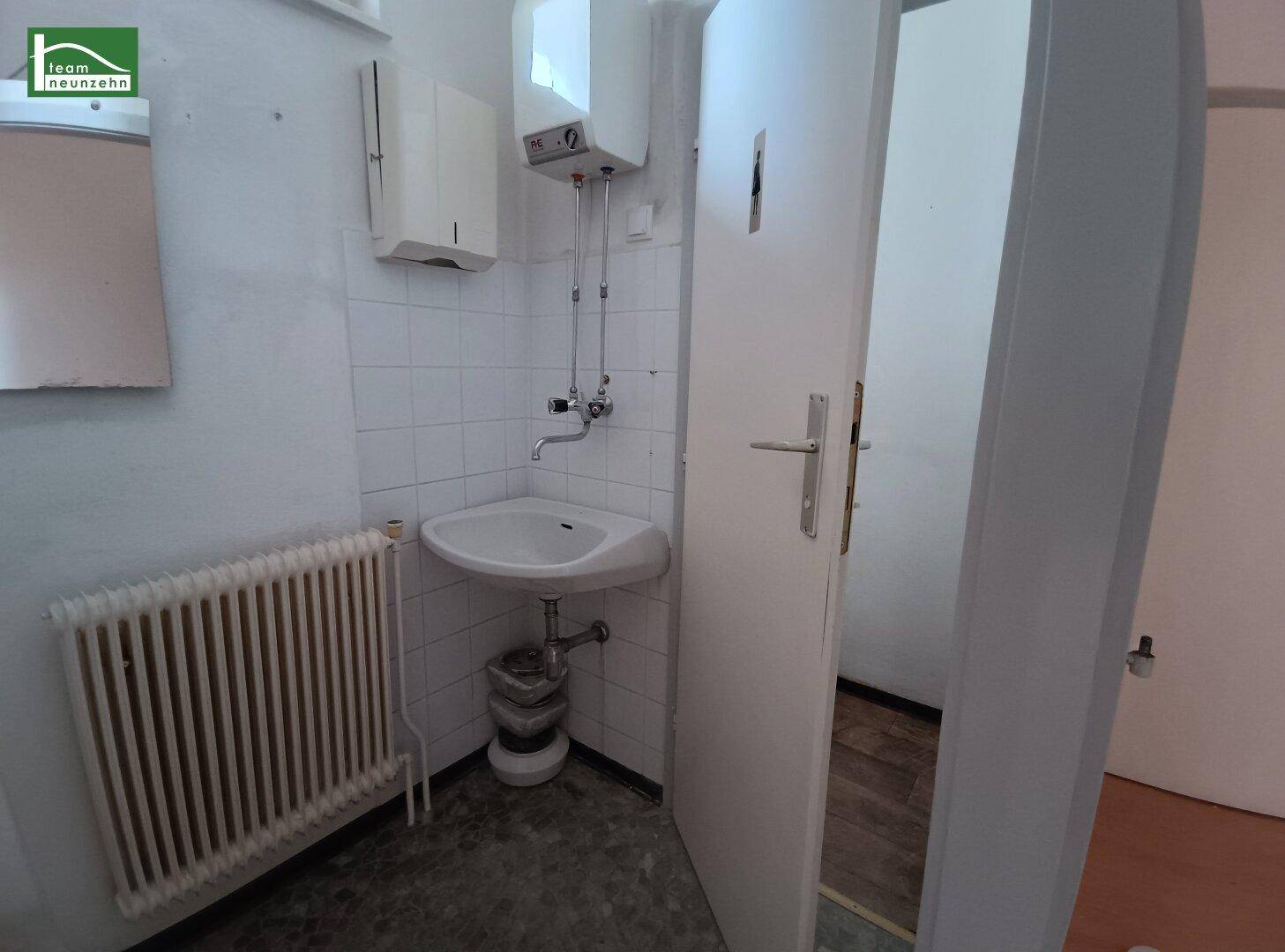 Einfacher Toilettenraum mit Waschbecken, Heizkörper und Wandfliesen.
