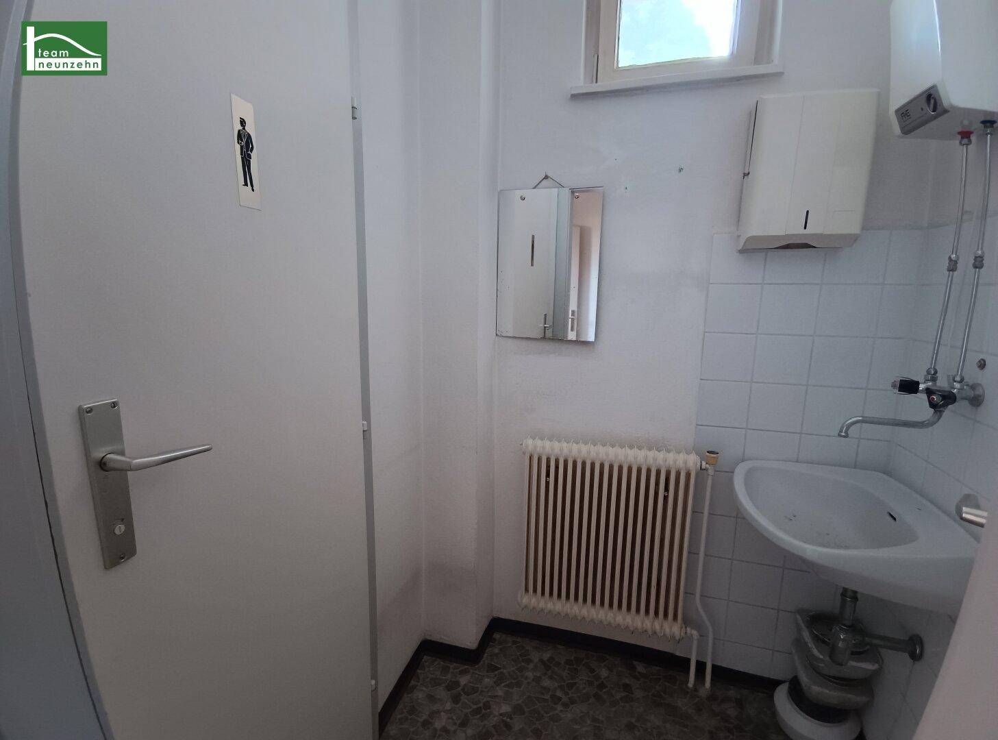 Kleiner Toilettenraum mit Waschbecken, Heizkörper, Spiegel und einem Fenster für Tageslicht.