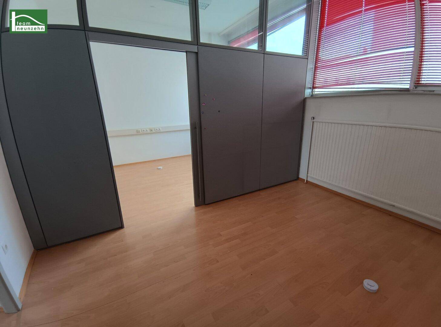 Heller Büroraum mit Laminatboden und einer grauen Trennwand mit Schiebetür.