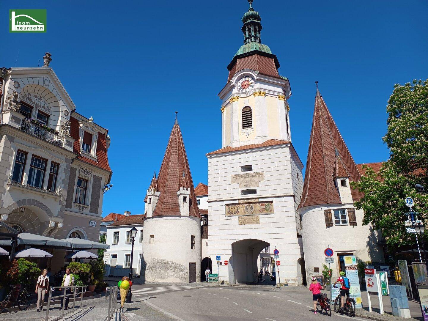 Historischer Stadtplatz mit einem markanten Uhrturm und traditionellen Gebäuden unter blauem Himmel.