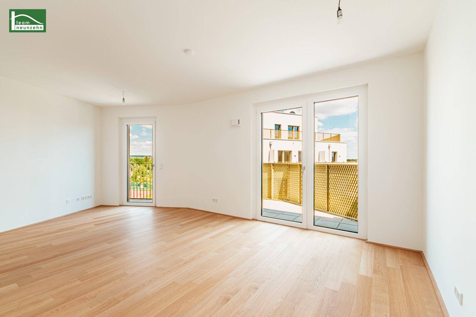 Geräumiges, helles Wohnzimmer mit Holzboden und Zugang zu zwei Balkonen.