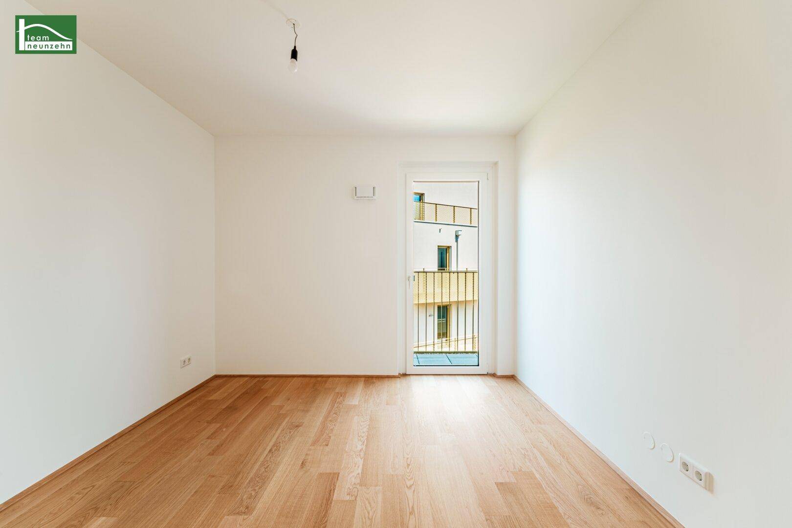 Helles, leeres Zimmer mit Holzboden und Zugang zu einem französischen Balkon.