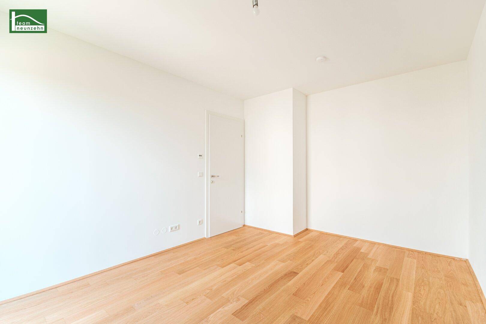 Leerer Raum mit hellen Wänden, Holzboden und einer weißen Innentür.
