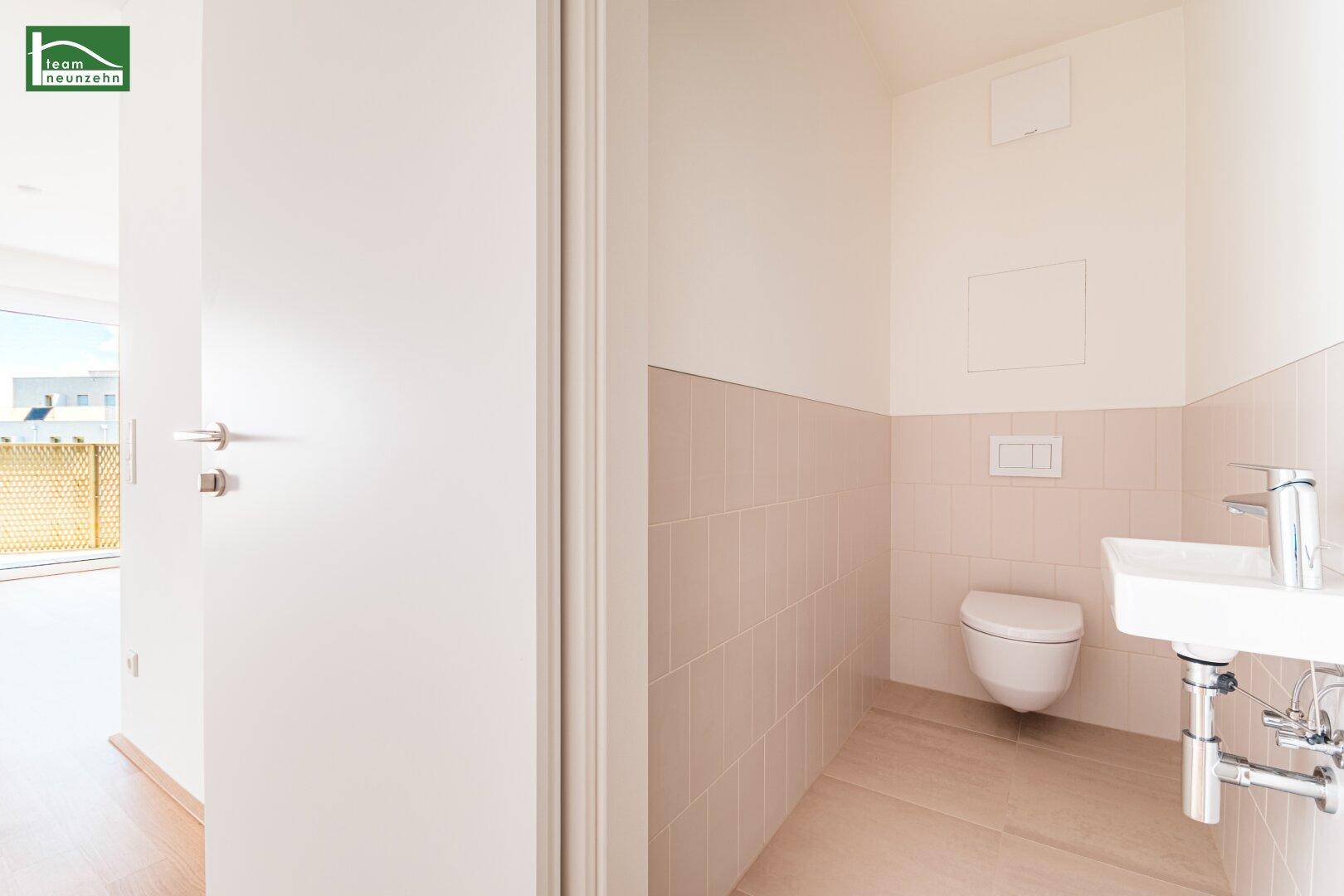 Separates Gäste-WC mit wandhängender Toilette und kleinem Waschbecken, halbhoch gefliest.
