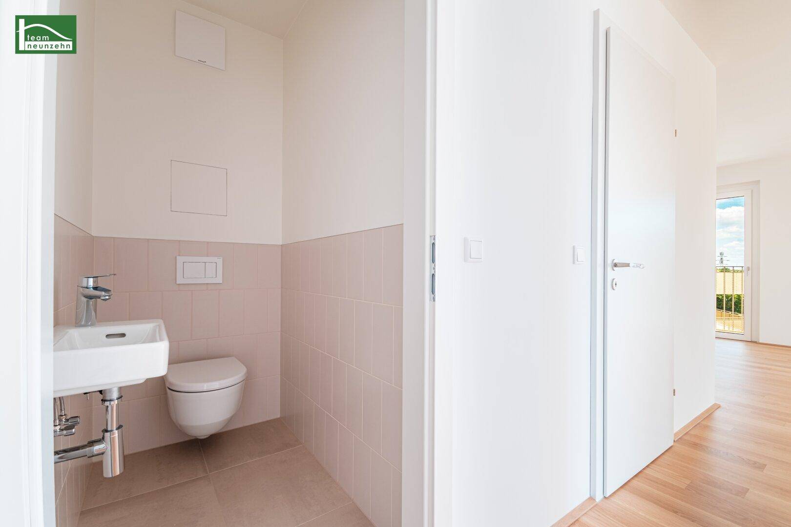 Separates Gäste-WC mit Wand-WC, kleinem Waschbecken und hellen Fliesen.