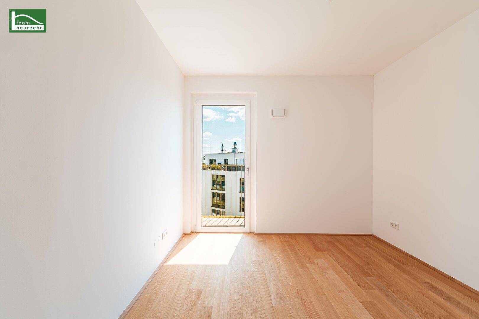 Sonniger Raum mit Holzboden und Fenstertür, die einen Blick nach draußen bietet.