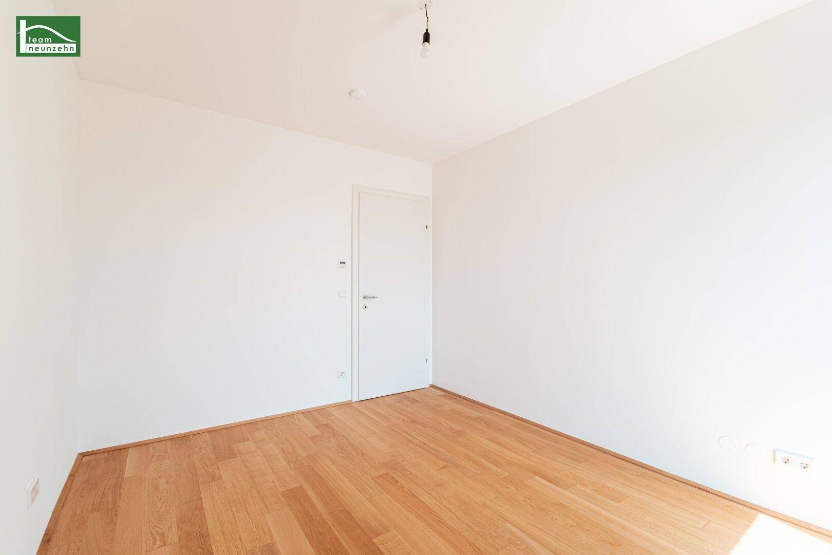 Helles, unmöbliertes Zimmer mit Holzboden und weiß gestrichenen Wänden.