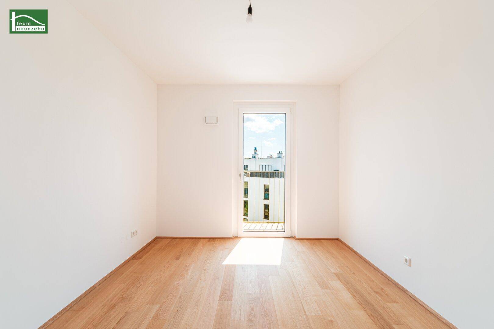 Leeres Schlafzimmer mit Parkettboden und Fenstertür, die viel Tageslicht hereinlässt.