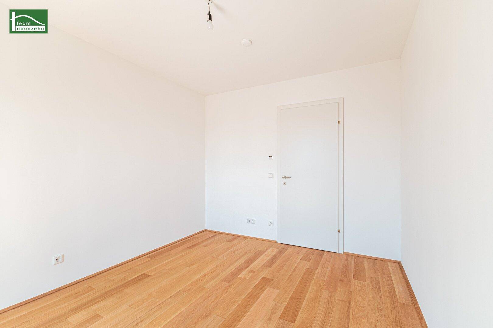 Geräumiges, leeres Zimmer mit Parkettboden und weißer Tür, bereit zur Einrichtung.