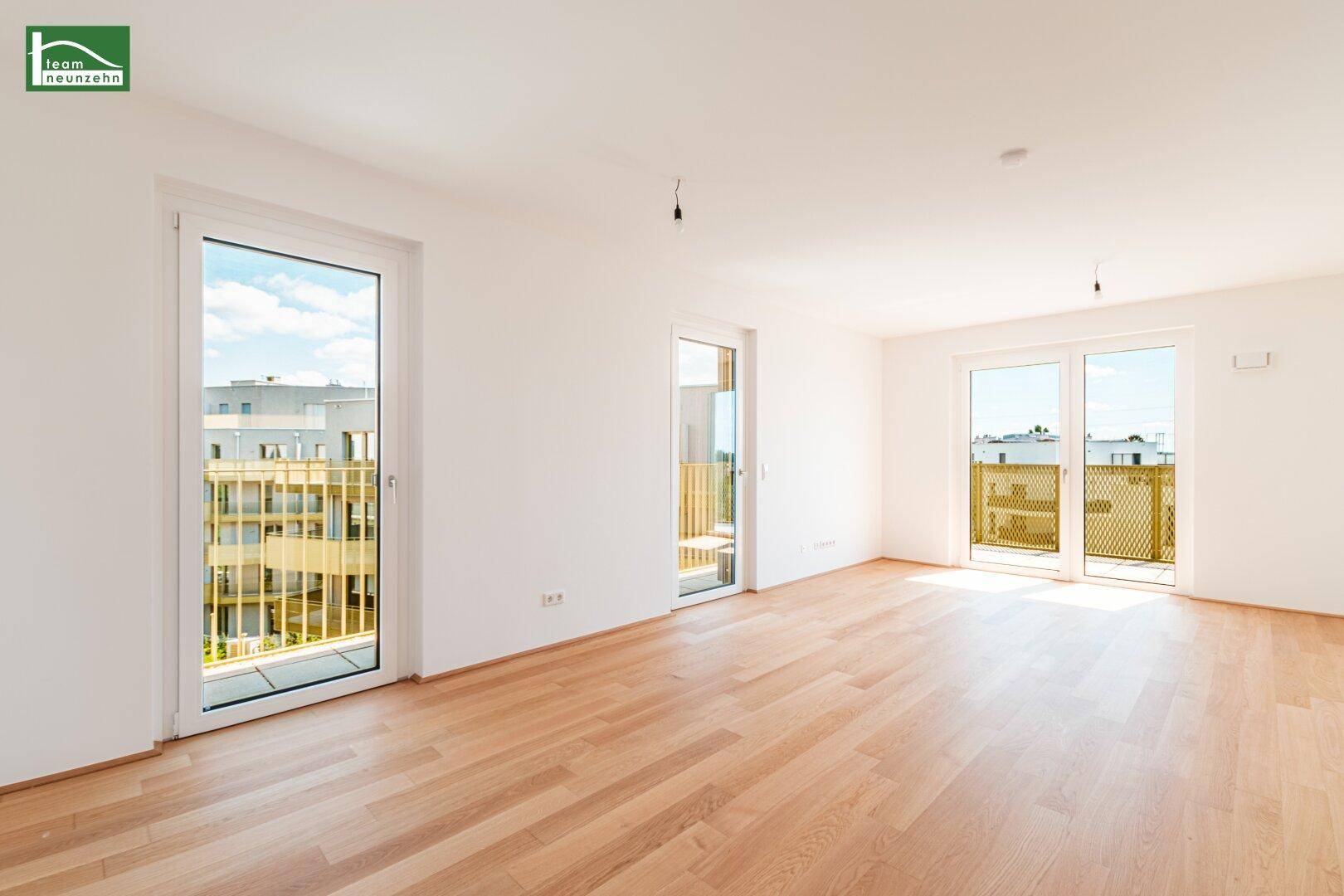Lichtdurchfluteter Wohnbereich mit Holzboden und mehreren Fenstertüren zu Balkonen.