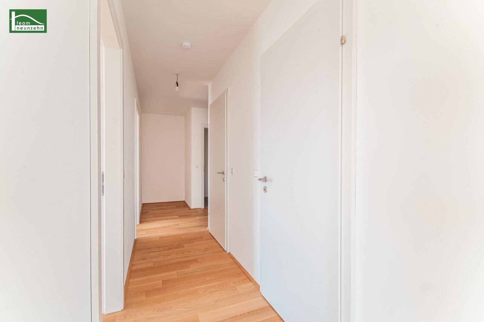 Heller Flur mit Holzboden und weißen Türen, der zu weiteren Räumen führt.