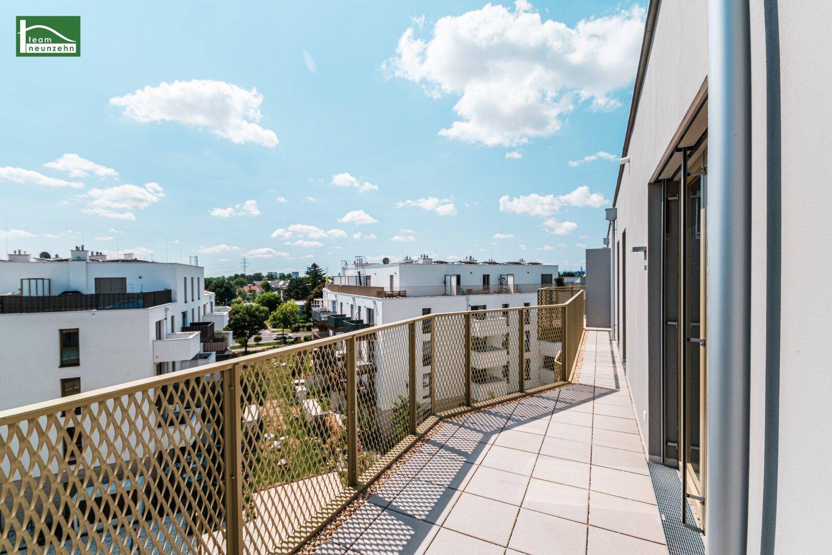 Breiter Balkon mit Gittergeländer und Blick auf die Nachbarschaft unter blauem Himmel.