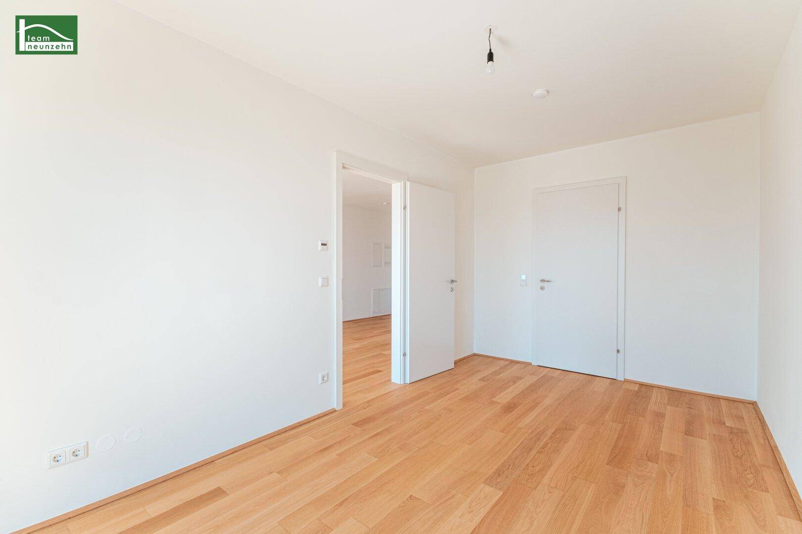 Geräumiges Zimmer mit Holzboden und zwei Türen zu angrenzenden Räumen, hell und einladend.