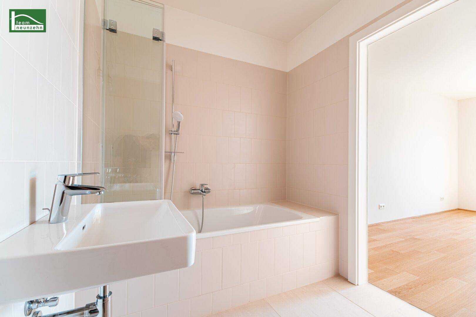 Helles Badezimmer mit Badewanne und Einzelwaschbecken, gefliest in sanften Beigetönen, mit Zugang zum Wohnbereich.