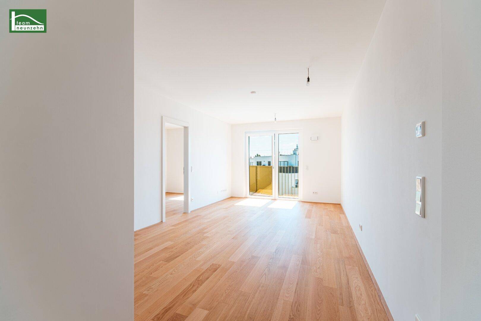Helles, leeres Zimmer mit Holzboden und Zugang zu einem Balkon, ideal für Wohnzwecke.