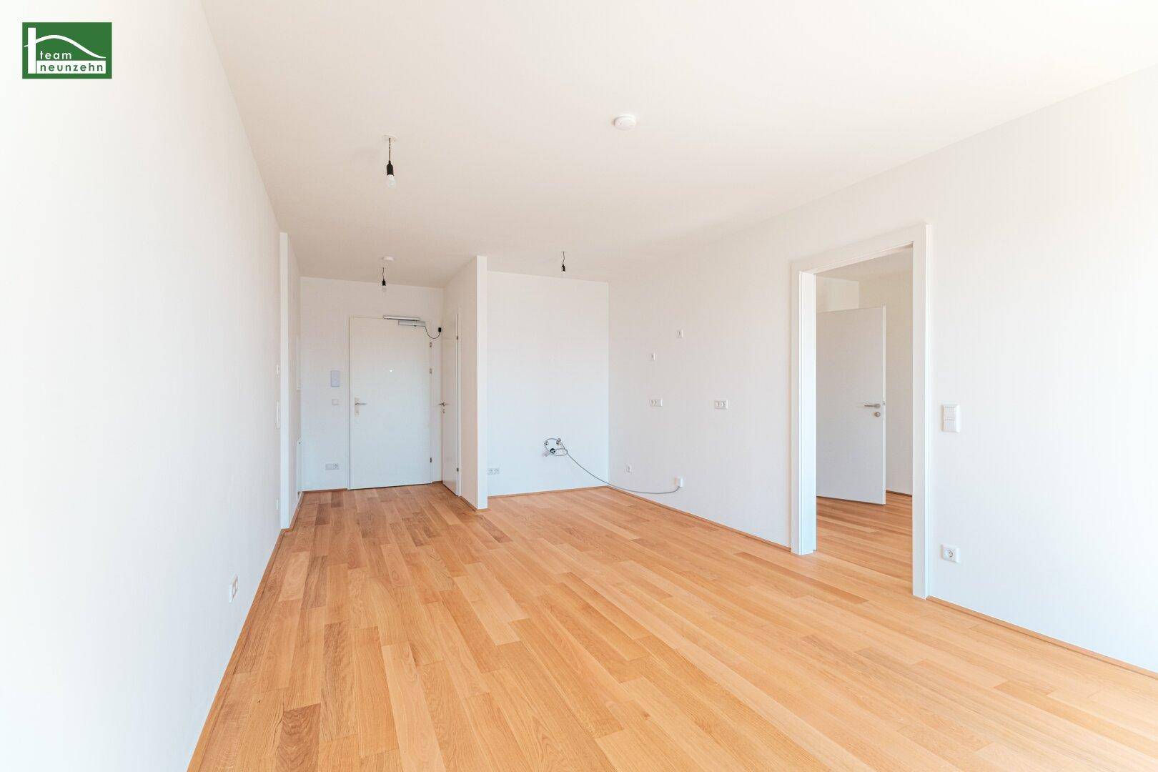 Heller Eingangsbereich mit Holzboden und weißen Wänden, der zu weiteren Räumen führt.
