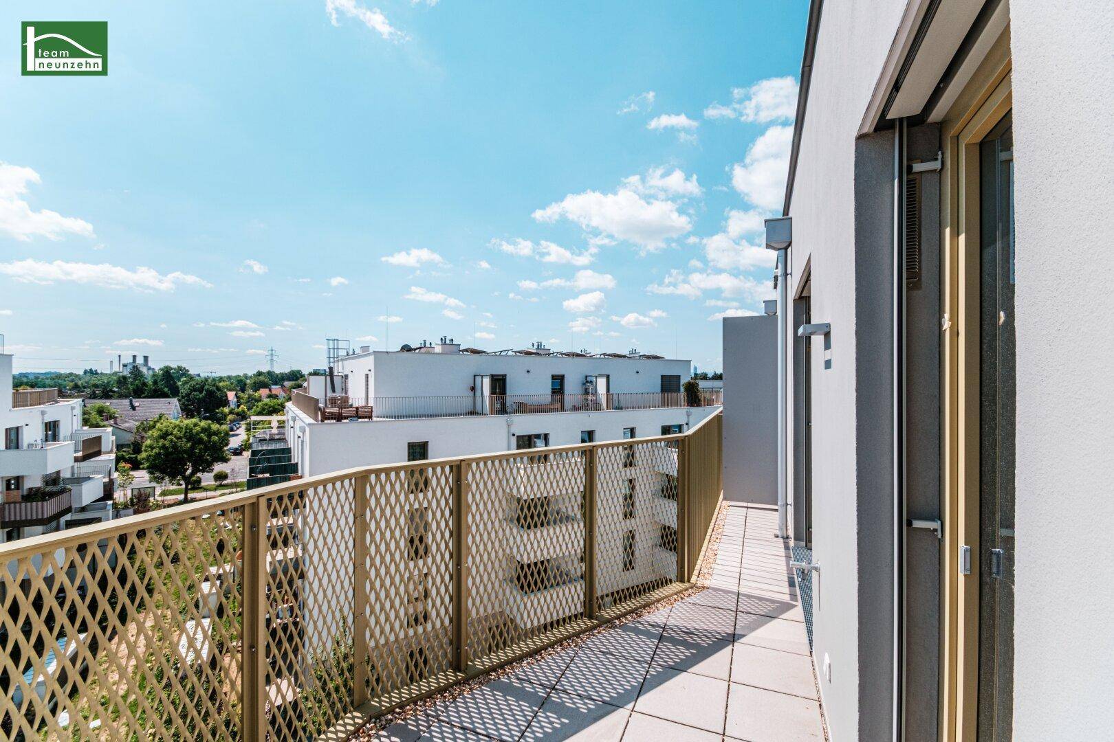 Sonniger Balkon mit Gitterbrüstung und weitem Blick über die moderne Wohnanlage.
