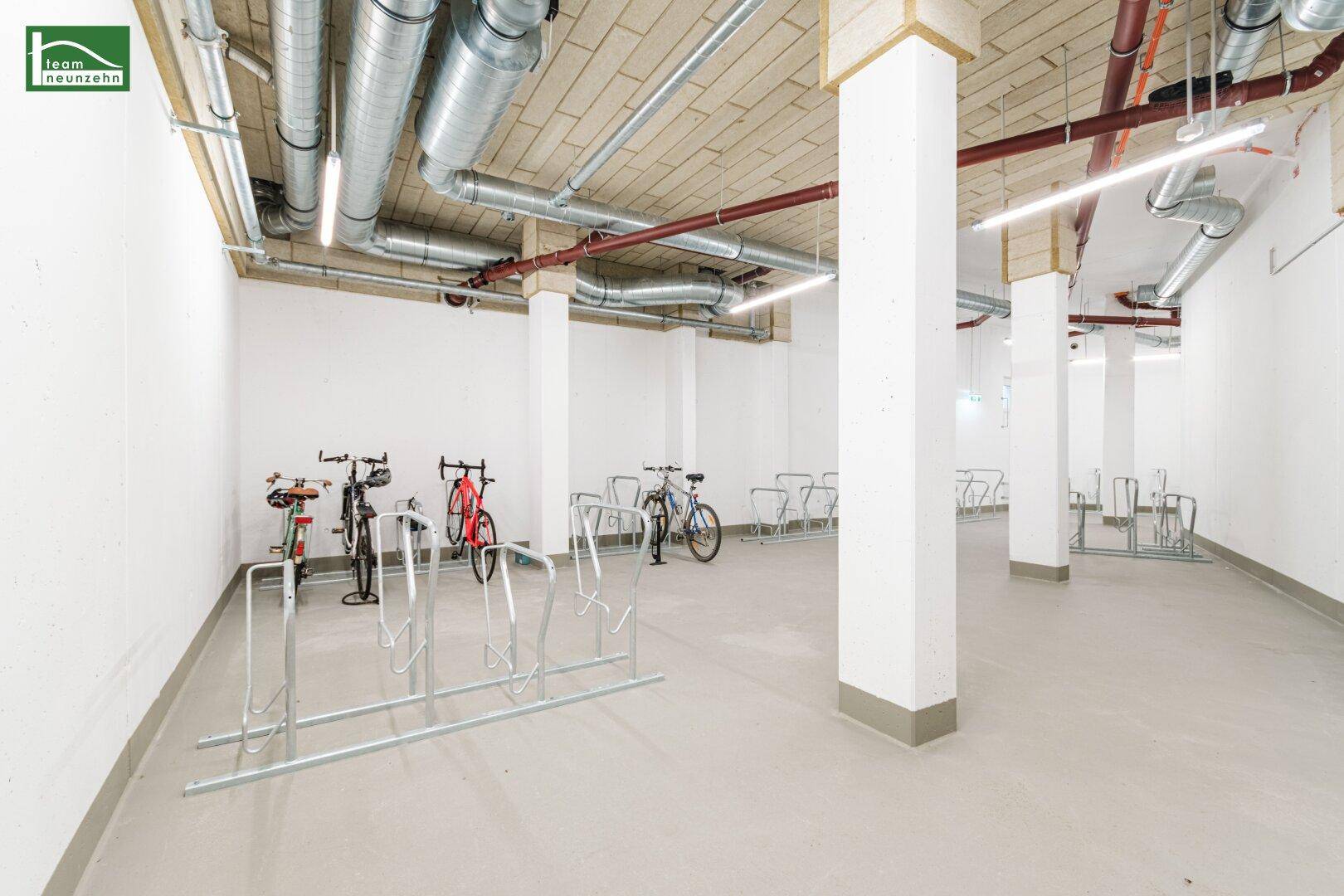 Geräumiger Fahrradraum mit zahlreichen Abstellmöglichkeiten und sichtbaren Installationen an der Decke.