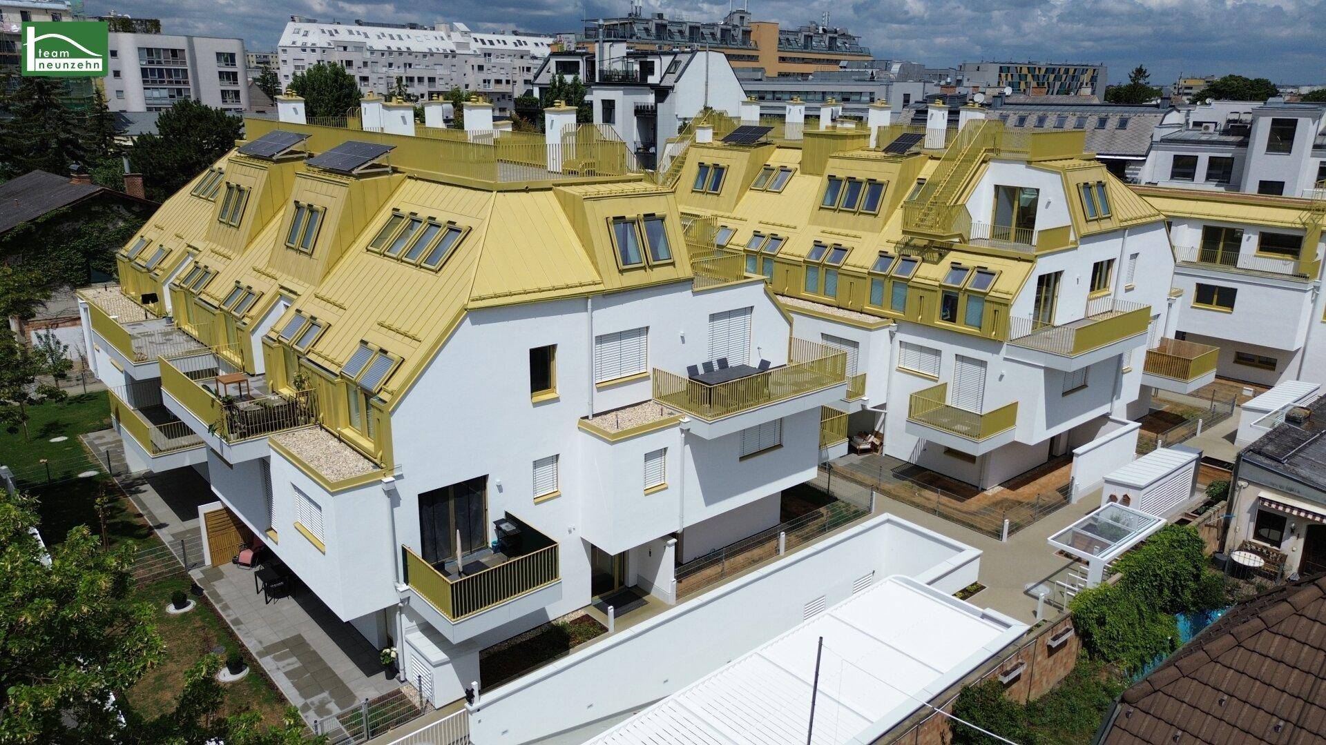 Luftaufnahme eines modernen Wohnkomplexes mit weißen Fassaden, goldenen Dächern und mehreren Balkonen.