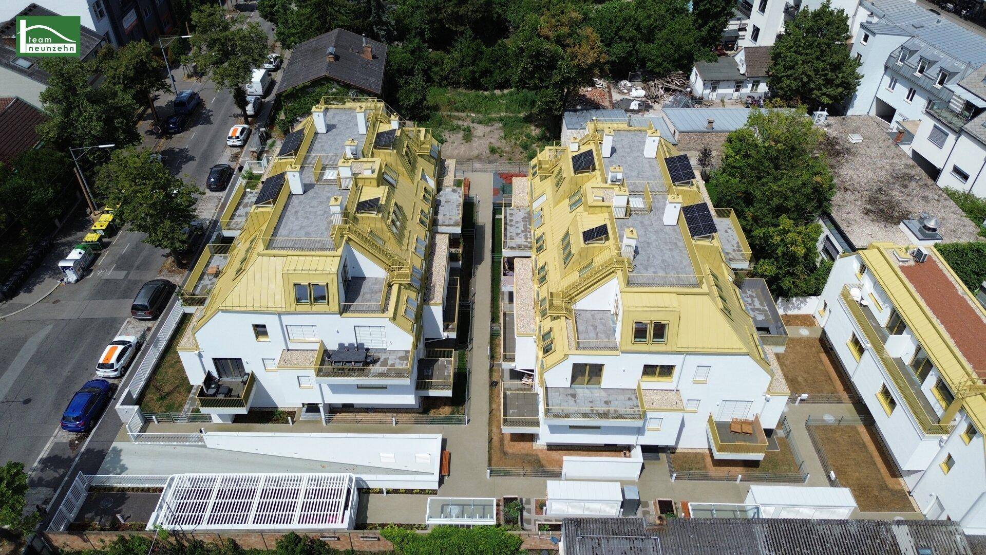 Luftaufnahme einer modernen Wohnanlage mit markanten goldfarbenen Dächern und Solarpaneelen in urbaner Umgebung.