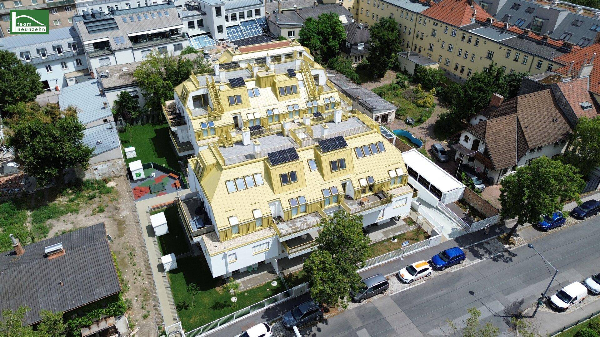 Luftaufnahme eines modernen Wohngebäudes mit goldfarbenem Dach und Solarpaneelen in städtischer Umgebung.